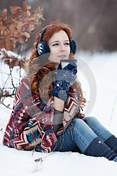 Dreamly young red-haired woman drinking a hot drink from a mug in the winter park.