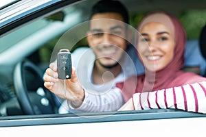 Dreams come true. Glad happy young arab husband and wife in hijab customers show keys at new car, close up