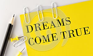 DREAMS COME TRUE word on the yellow paper with office tools on white background