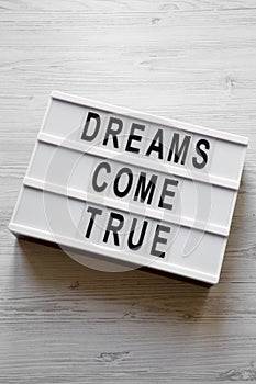 `Dreams come true` words on lightbox over white wooden surface, overhead