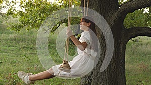 Dreams of flying. free girl swinging on a swing on an oak branch in sun. Happy childhood concept. Beautiful girl in a