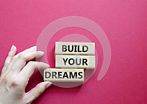 Dreams symbol. Concept word Build your Dreams on wooden blocks. Businessman hand. Beautiful red background. Business and Build