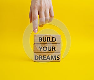 Dreams symbol. Concept word Build your Dreams on wooden blocks. Businessman hand. Beautiful yellow background. Business and Build