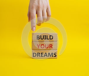 Dreams symbol. Concept word Build your Dreams on wooden blocks. Businessman hand. Beautiful yellow background. Business and Build