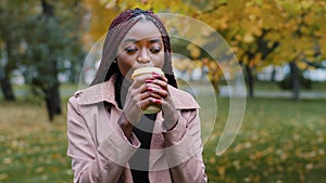 Dreamy African American young woman drinking coffee or tea in disposable cup, brooding millennial student girl enjoying