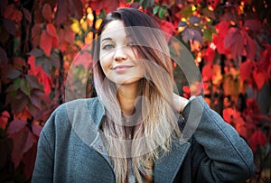 Dreamy beautiful girl with long colorful hair on autumn background of red grape hedge. Inspired woman in gray coat. Autumn