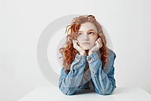 Dreamy beautiful girl thinking dreaming sitting at table over white background.