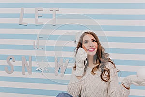 Dreamy blue-eyed young girl in New Year`s mood posing sitting on floor in studio decorated with inscription.