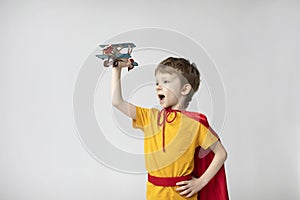 Dreamy boy in a red cape plays with an airplane toy