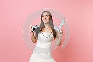 Dreamy bride woman in wedding dress looking up hold retro vintage photo camera and check mark, choosing staff