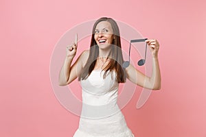 Dreamy bride woman in wedding dress pointing index finger up hold musical note choosing staff, musicians or DJ isolated