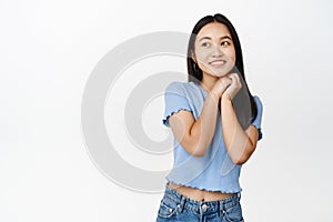 Dreamy brunette asian girl thinking, yearning for something, smiling and gazing aside, standing over white background