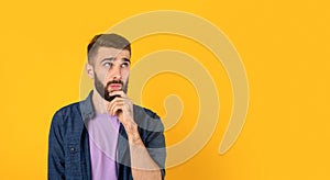 Dreamy Caucasian guy thinking over something, touching his chin on orange background, banner design with copy space