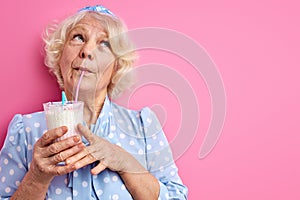 dreamy caucasian senior woman drinking milk cocktail isolated