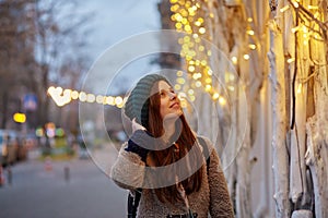 Dreamy caucasian woman walking in the street. City lights. Winter casual clothes. Festive city at the evening. Copy