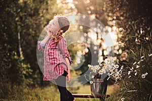 Dreamy child girl in plaid dress on the walk in summer day with bouquet of chamomile flowers