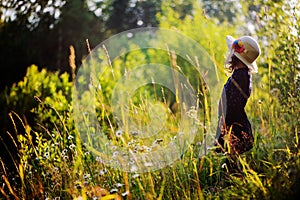 Dreamy child girl on summer walk on riverside. Cozy rural scene. Outdoor activities