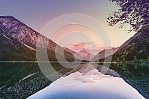 dreamy, colorful evening mood on the smooth, mirrored natural lake plansee in tyrol with a house on a slope and mountains