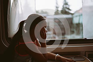 Dreamy, contemplative tourist girl in cozy and comfortable train looking out window, journey. Vacation or summer camp