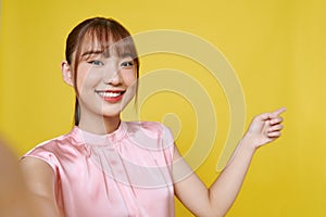 Dreamy cute young lady recording self video showing arm empty space isolated on yellow background