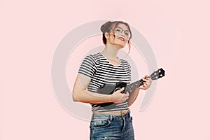 Dreamy eccentric lady in striped shirt playing ukulele. Over pink background.
