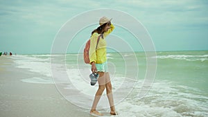 Dreamy freedom woman in summer bright clothes with small backpack arms walking at seaside, enjoying storm windy weather