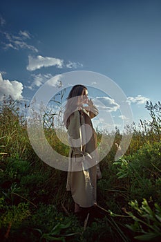 Dreamy gentle woman in a beige raincoat in nature. Romantic young woman in thick tall grass in field. Natural beauty, enjoyment of