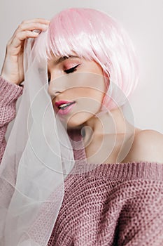 Dreamy girl with bright makeup posing on light background in pink periwig with eyes closed. Studio shot of shy pretty