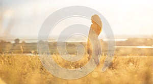 Dreamy girl in a field at sunset, a young woman in a haze from the sun enjoying nature, romantic style