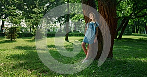 Dreamy girl lean tree trunk in park. Smiling kid observing nature around