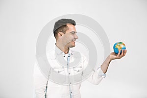 Dreamy handsome smiiling man with globe in hand thinks about which new country to visit, where to travel, isolated over