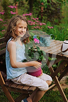 dreamy happy child girl relaxing in summer evening garden with geranium flower in pot