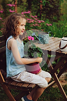 Dreamy happy child girl relaxing in summer evening garden with heranium flower in pot