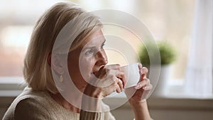 Dreamy happy middle aged woman looking away drinking morning coffee