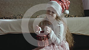 A dreamy little girl wearing Santa's hat is holding a lantern with burning candle. The concept of hope, holiday