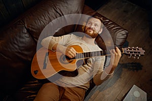 Dreamy man lying on couch playing guitar