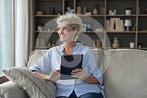 Dreamy mature woman enjoy carefree pastime using digital tablet