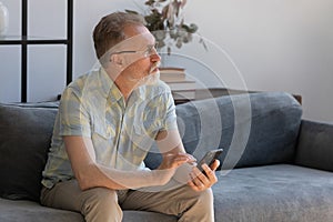 Dreamy old retired man using cellphone at home.