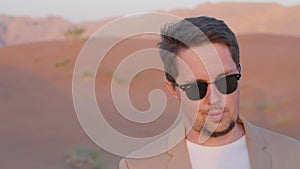 Dreamy pensive businessman in sunglasses enjoying red desert in UAE.