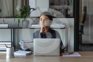 Dreamy pensive young indian ethnic businesswoman thinking of career challenges.