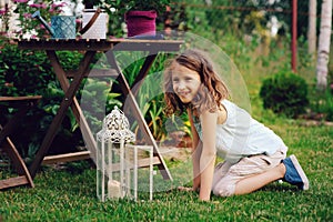 Dreamy romantic kid girl relaxing in evening summer garden decorated with lantern