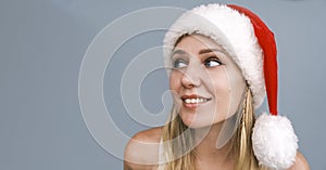 Dreamy smiling Santa girl wearing red hat looking side up. Portrait of beautiful young blue-eyed blonde woman in