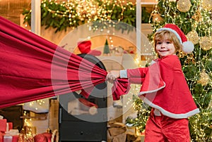 Dreamy toddler on Christmas eve. For Christmas and New Year posters. Santa helper holding a red bag with presents. Santa