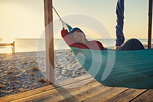 Dreamy woman relaxes in a hammock on abandoned bungalow