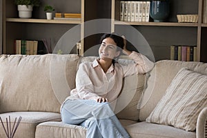 Dreamy woman relaxing on sofa in living room staring aside