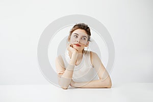 Dreamy young beautiful girl student sitting at table dreaming thinking over white background.