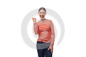 dreamy young brunette woman dressed in a tight-fitting orange sweater rejoices and holds her fist up