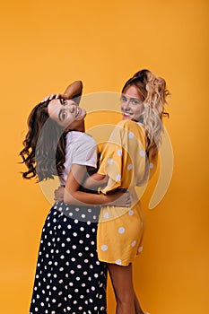 Dreamy young sisters playfully looking back. Indoor photo of stylish female friends posing with cute smile..