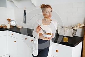 Dreamy young woman eating cereals with milk on home kitchen