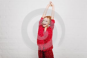 Dreamy young woman with pleased face expression stretching in morning. Cute european girl enjoying photoshoot in red